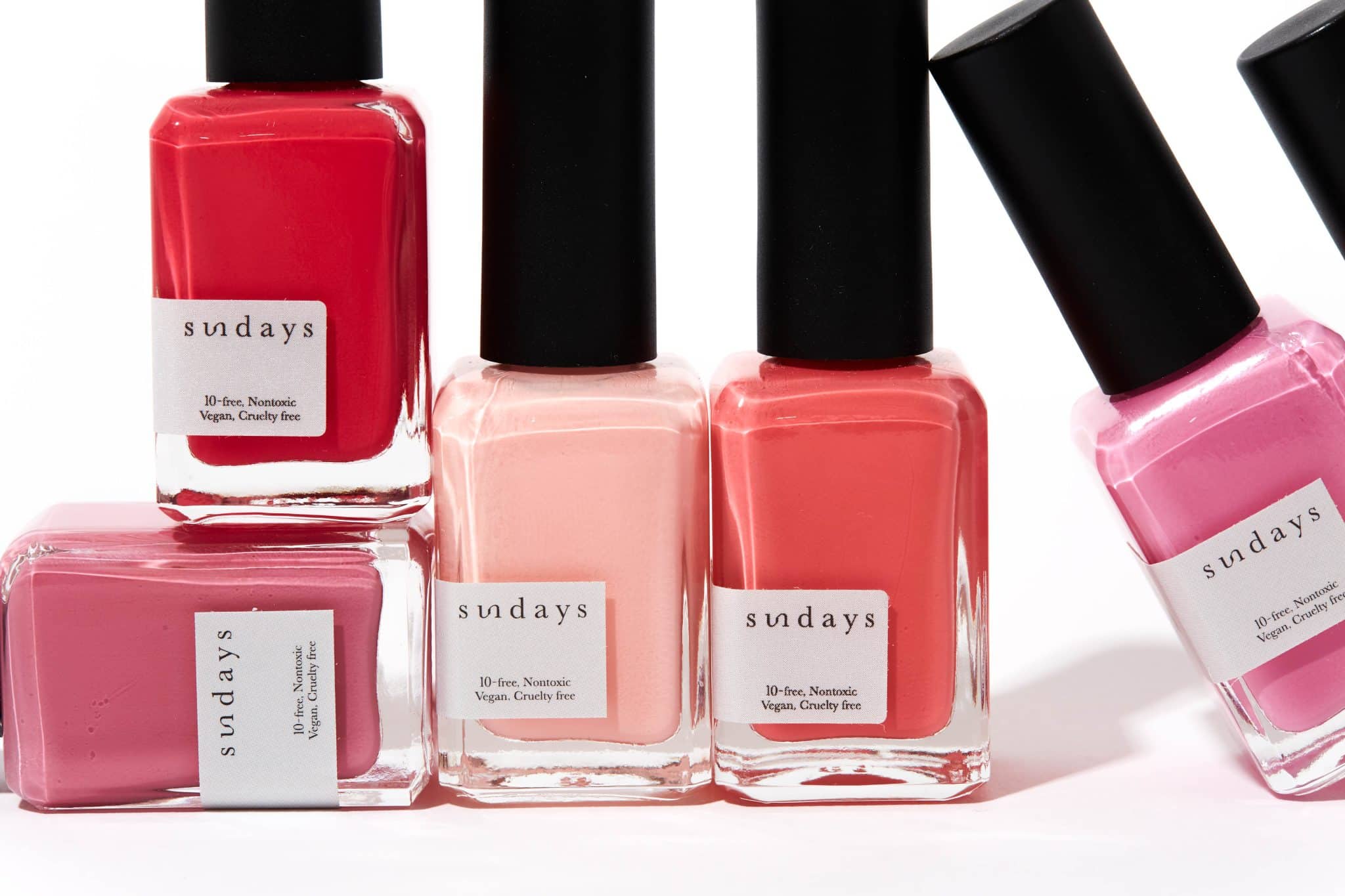 a stack of sundays studio red and pink nail polish bottles