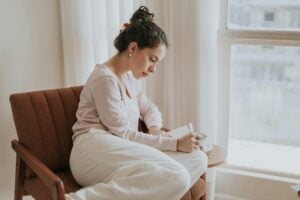 Woman writing a journal while sitting by the window.