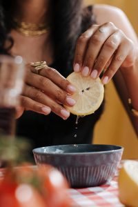 close-up of woman, wearing pink nail polish, holding a lemon over a bowl