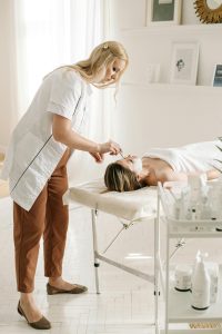 Esthetician standing while giving a facial to a woman lying on a massage table in a bright, peaceful, and homey treatment room.