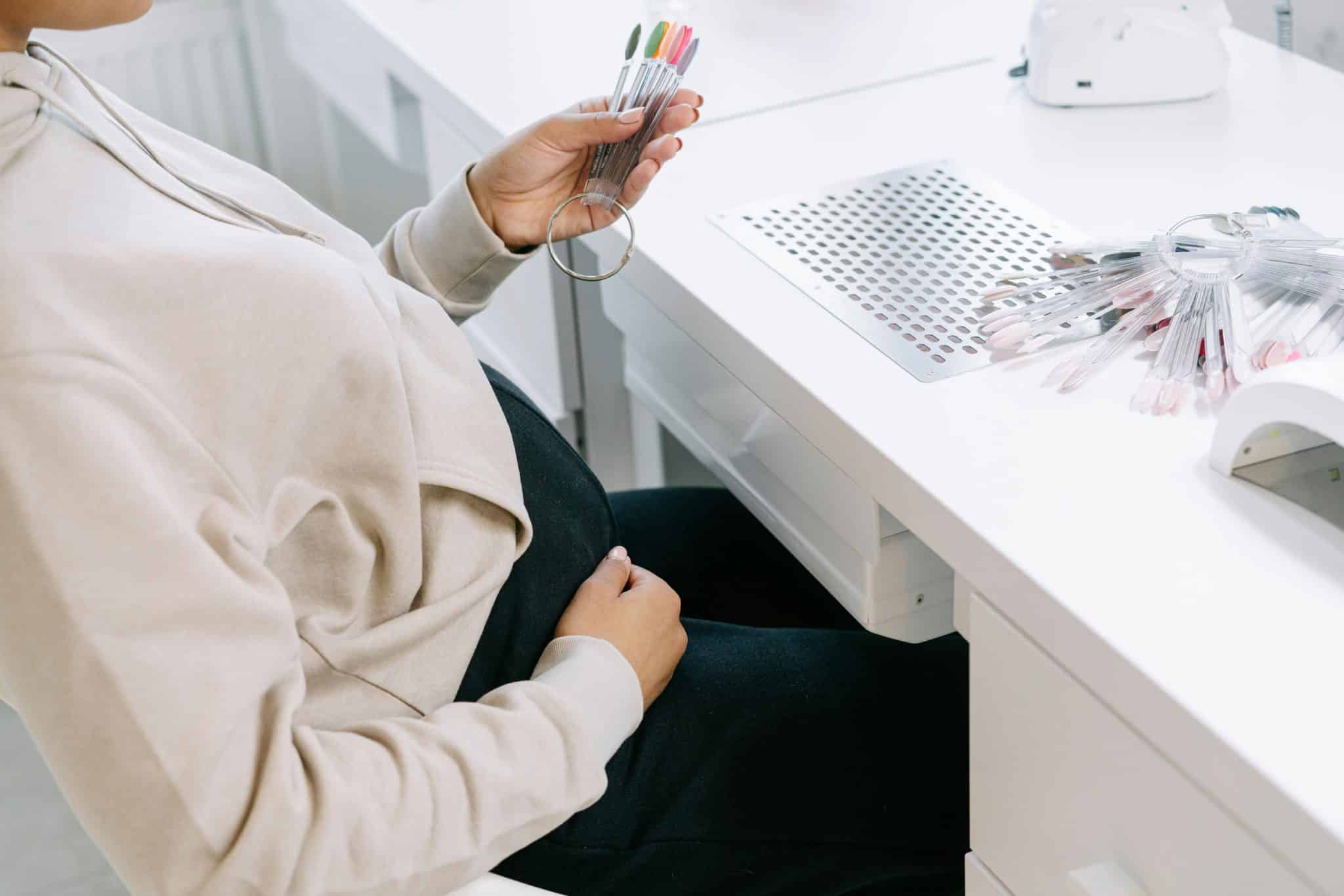 pregnant woman sitting down and choosing nail polish color at nail salon