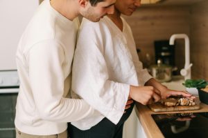 pregnant woman chopping mushrooms on kitchen counter top while being embraced by her partner