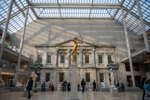 Interior view of the Metropolitan Museum featuring a glass ceiling and a prominent gold statue displayed on a central pedestal.