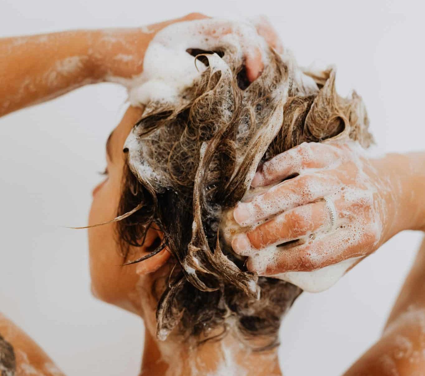 Back profile of woman with wet hair and shampoo suds in a clean, white shower