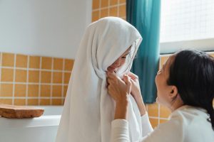 Child wrapped in a towel by mother after getting out of the bath in a bathroom with deep yellow tile and turquoise curtains.