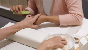 woman receiving a sundays studio rose anti-aging manicure with one hand being filed and the other soaking in a rose petal bath