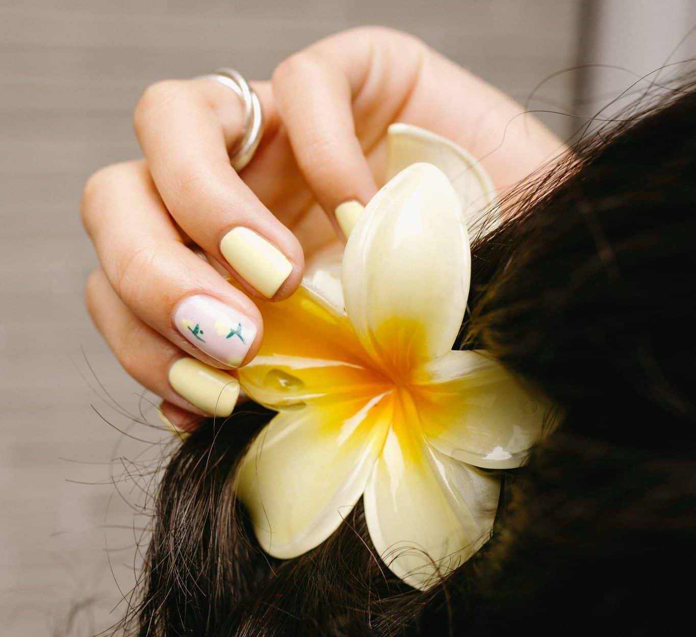 close-up of hand with yellow painted nails grabbing yellow plumeria hair clup