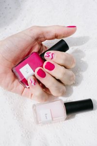 woman holding pink nail polish bottle with a lighter pink nail polish bottle next to her hand