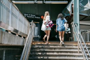 Two women in summer attire entering the NYC subway, carrying roller skates