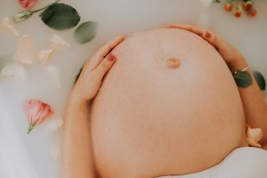 a pregnant woman in a milky, flower-filled bath, with her hands on her baby bump