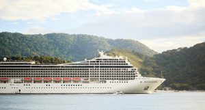Cruise boat in the ocean, in front of rolling green mountains