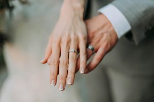 hand of a bridge over the hand of the groom, both with their wedding rings on