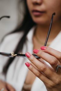 Woman in white button up with deep pink nails holding sun glasses