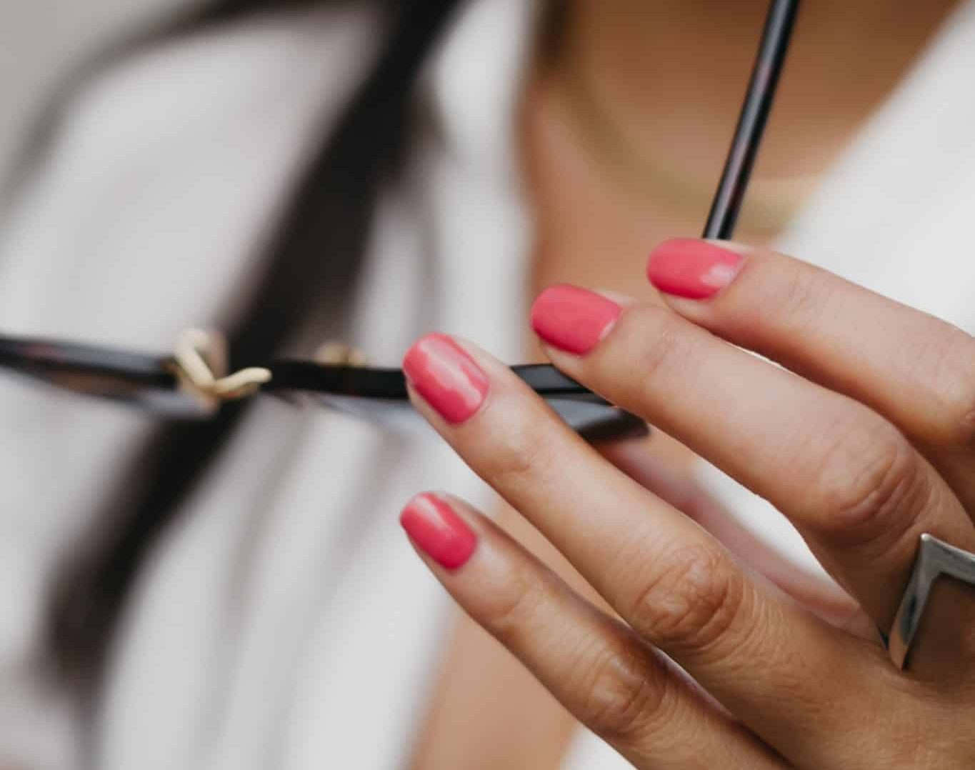 Woman in white button up with deep pink nails holding sun glasses