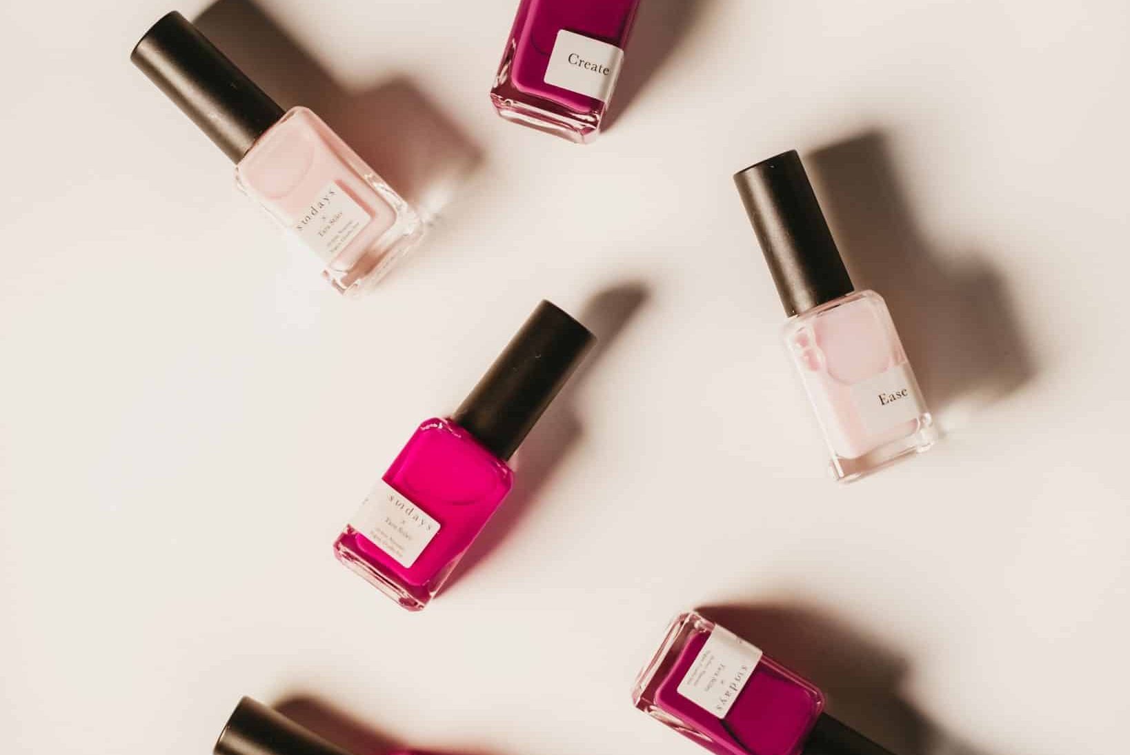 6 Nail polish bottles of different shades of pink laying flat against off-white background.