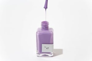 Purple nail polish bottle with removed cap and polish dripping into the bottle.
