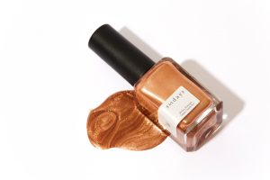 Gold nail polish bottle spilled over onto white surface