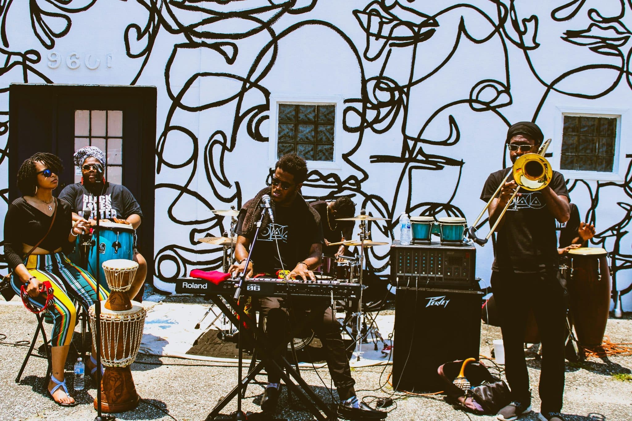 Black band playing together outside in front of a mural wall