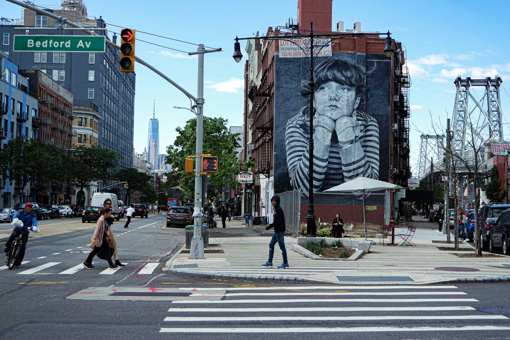 street view of a black and white mural of a girl with her chin on her hands on the side of a building on Bedford Ave, Brooklyn, New York.