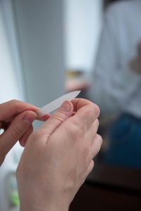 Close up of someone filing their bare nails with living room setting blurred in the background.
