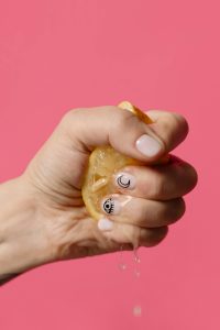 Hand with moon and eye nail art squeezing a lemon in front of a pink wall