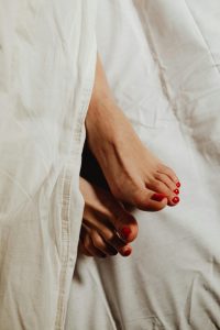 Womans toes with red nail polish peeking through white linen sheets