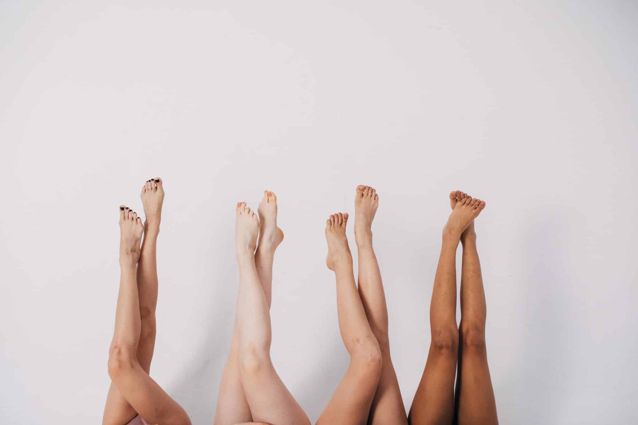 The legs of four women with pedicures in front of a white wall.