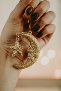 Woman with black nail polish on her fingernails holding a gold moon and star ornament 
