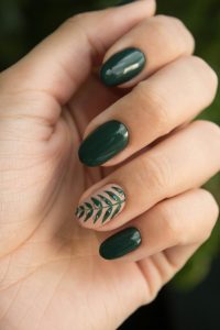 Close up of a woman's nails with green on all fingers except the ring finger, which features a green leaf design