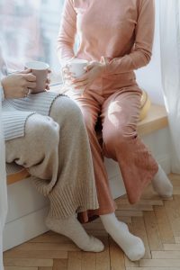 Two Persons Wearing Loungewear Holding a Cup of Coffee while Sitting by the Window