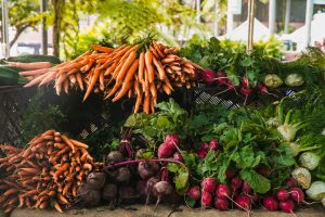 Farm stand with bunches carrots, radishes, and beets on a wooden table.