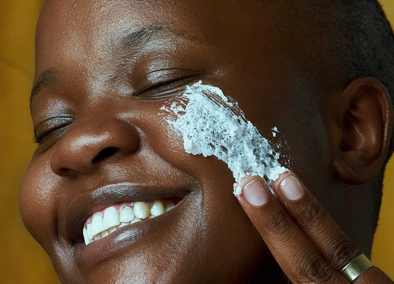 black woman applying white sunscreen or cream on face while smiling