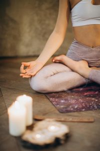 woman sitting in padmasana on a yoga mat with candles nearby