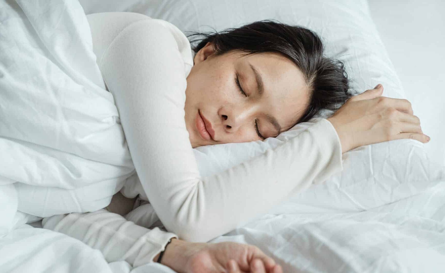 Woman in white longsleeve sleeping in bed with white sheets