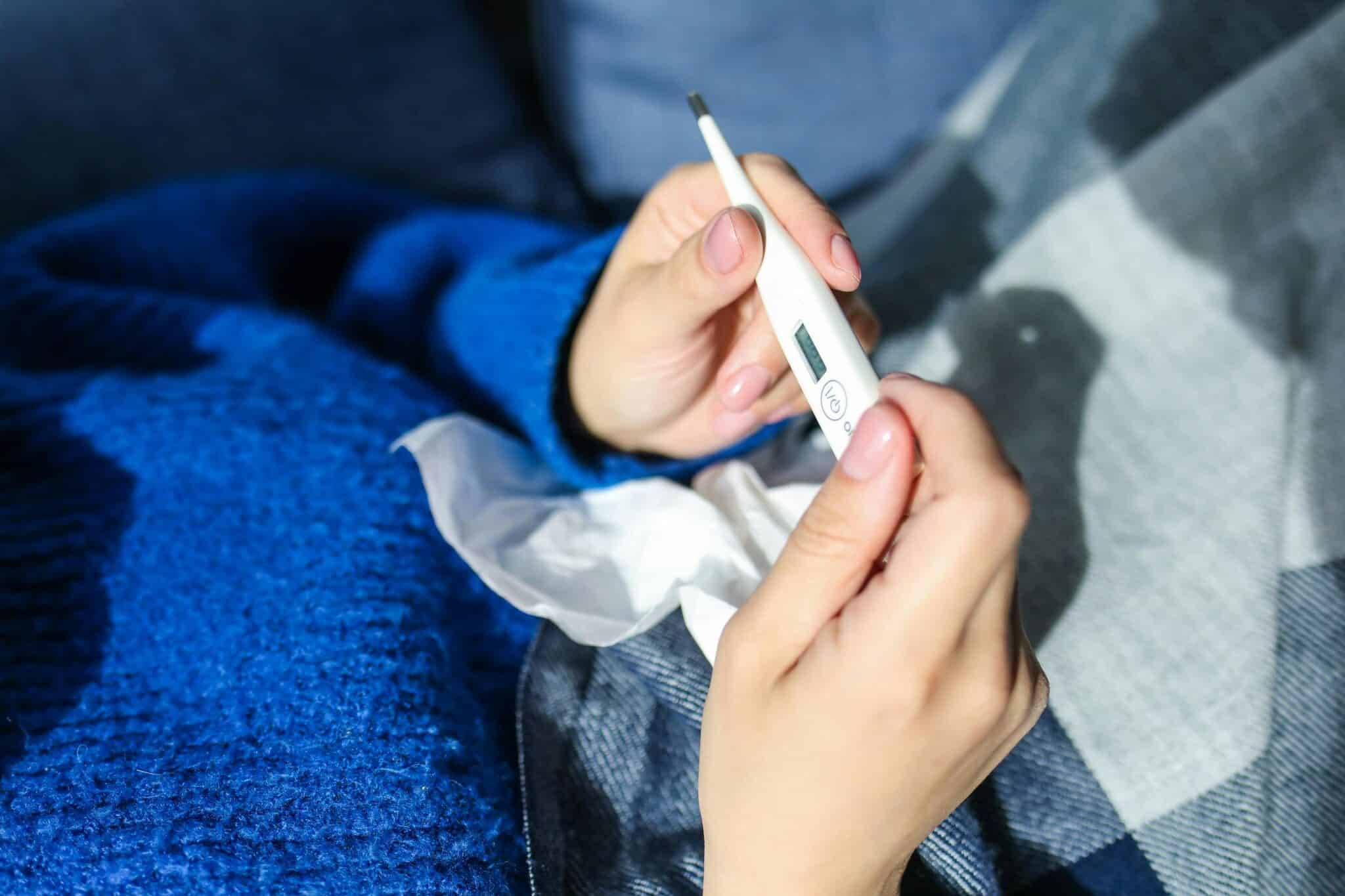 Close up of woman in blue sweater checking her temperature with on a white thermometer